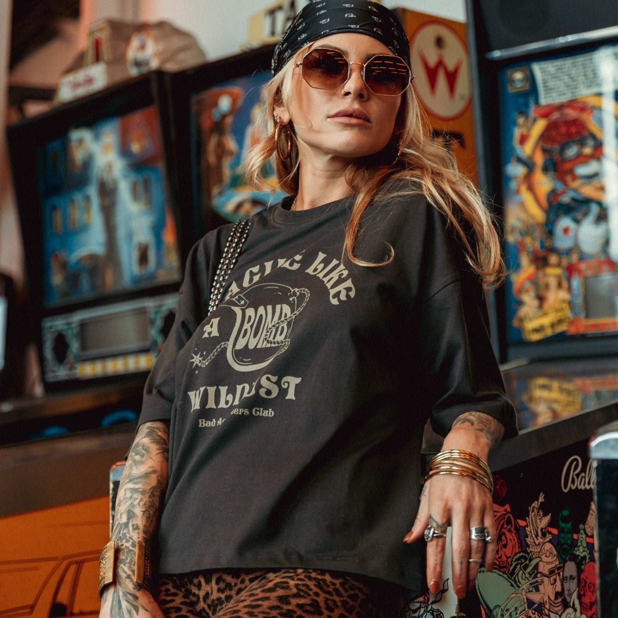 a young woman by game machines wearing off-black wide cut short sleeve women's motorcycle t-shirt with helmet motive and Fragile like a bomb  logo 