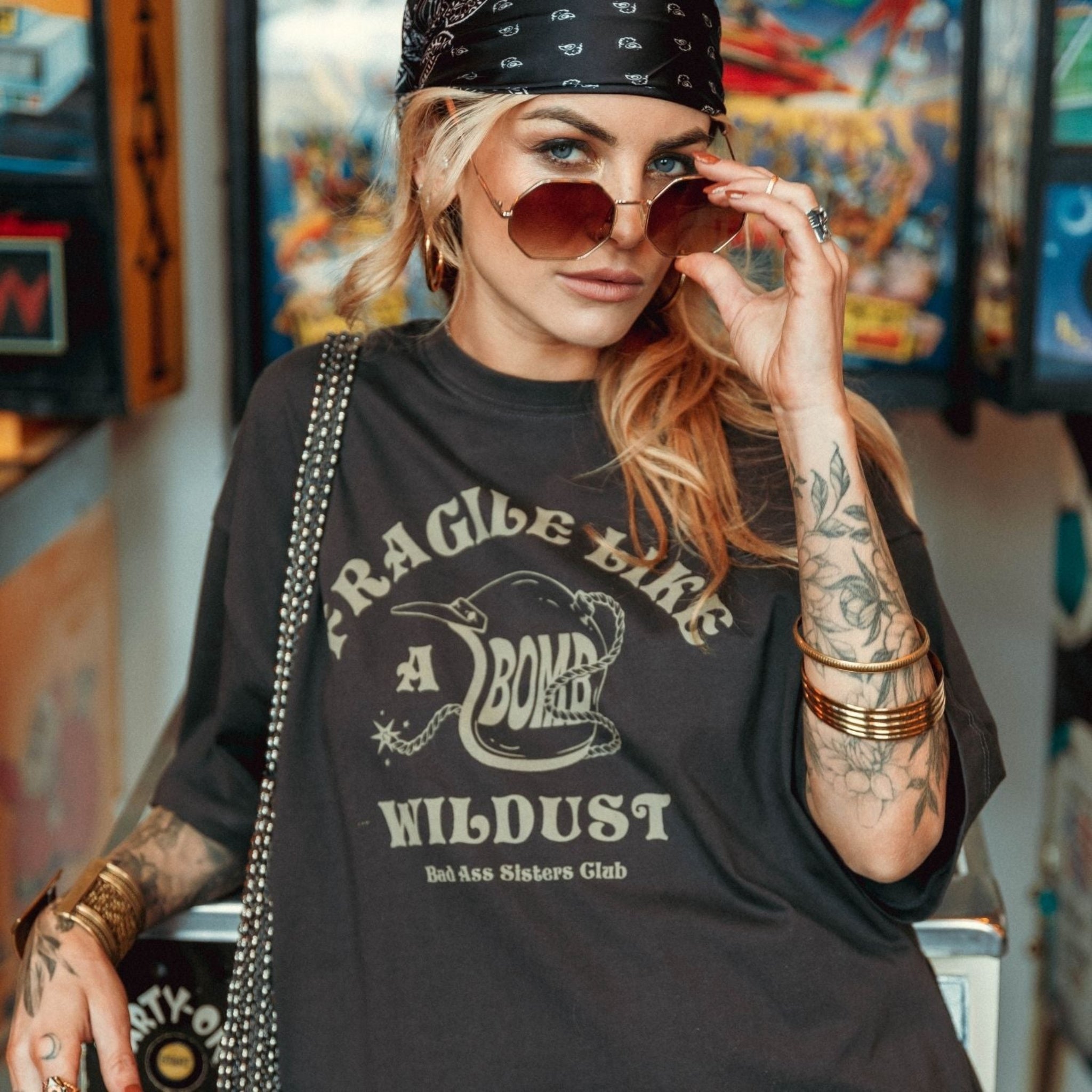 a young woman with sunglasses wearing off-black wide cut short sleeve women's motorcycle t-shirt with helmet motive and Fragile like a bomb  logo 