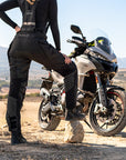 A woman standing by her motorcycle wearing Black SHIMA touring motorcycle pants for women 