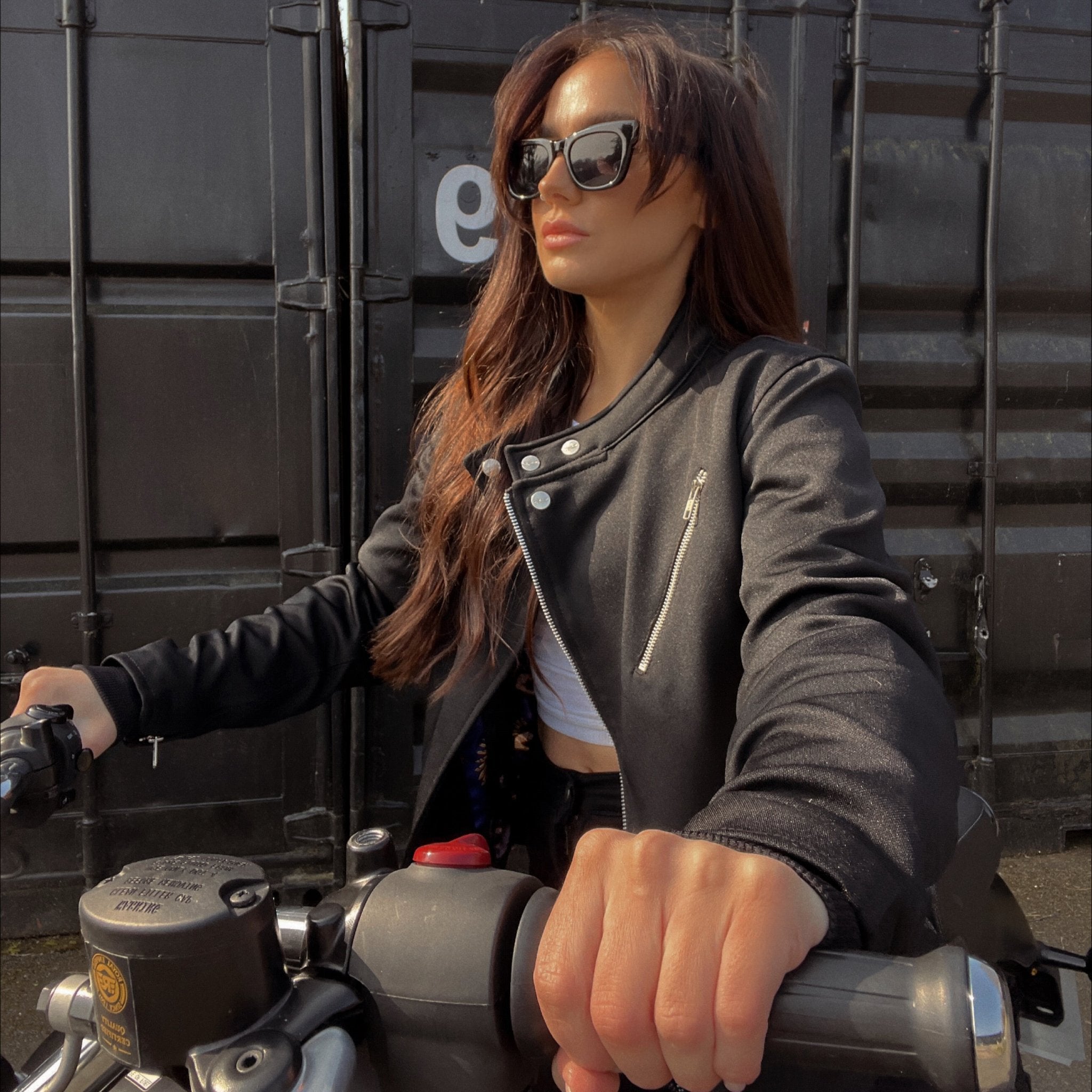 a young lady on a motorcycle wearing Black retro style woman's motorcycle jacket with silver zip details