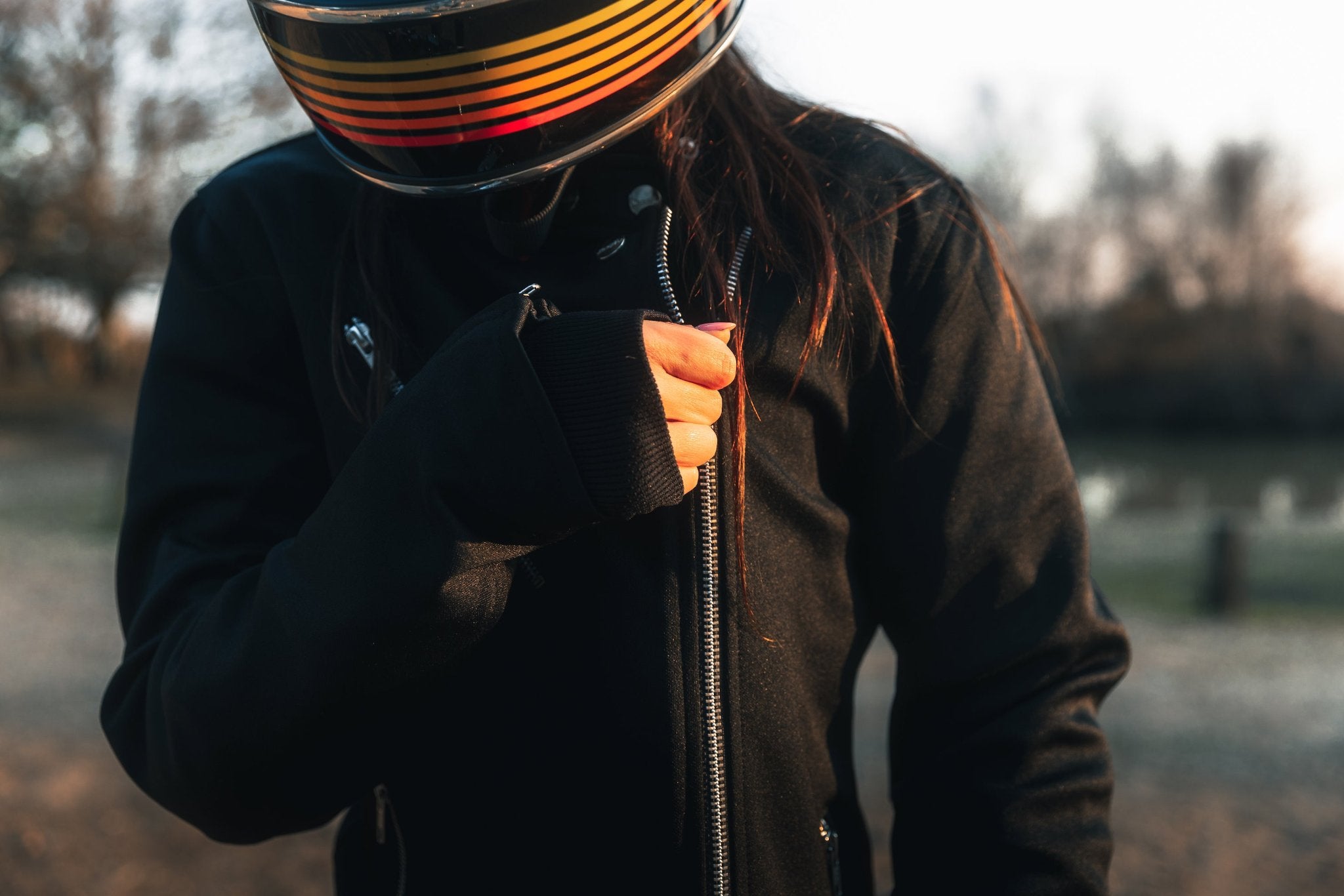 woman with a helmet zipping her Black retro style woman&#39;s motorcycle jacket with silver zip details