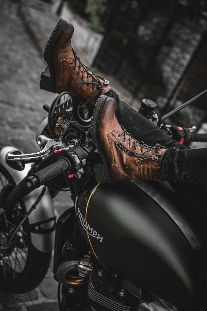 women&#39;s feet resting on motorcycle steering wheel, wearing brown leather mc boots 