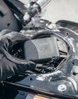 A motorcyclist's hand placing MoniMoto Motorcycle black and small GPS tracker into the motorcycle