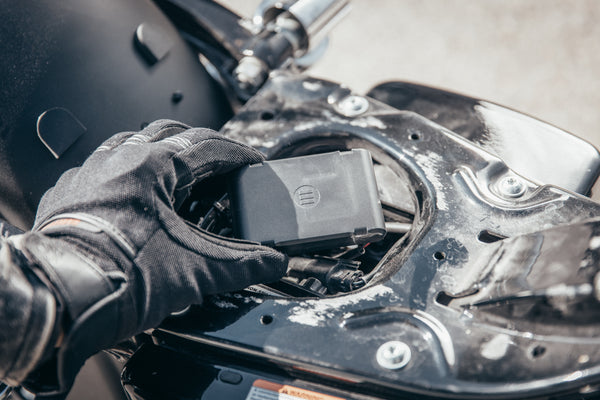 A motorcyclist's hand placing MoniMoto Motorcycle black and small GPS tracker into the motorcycle