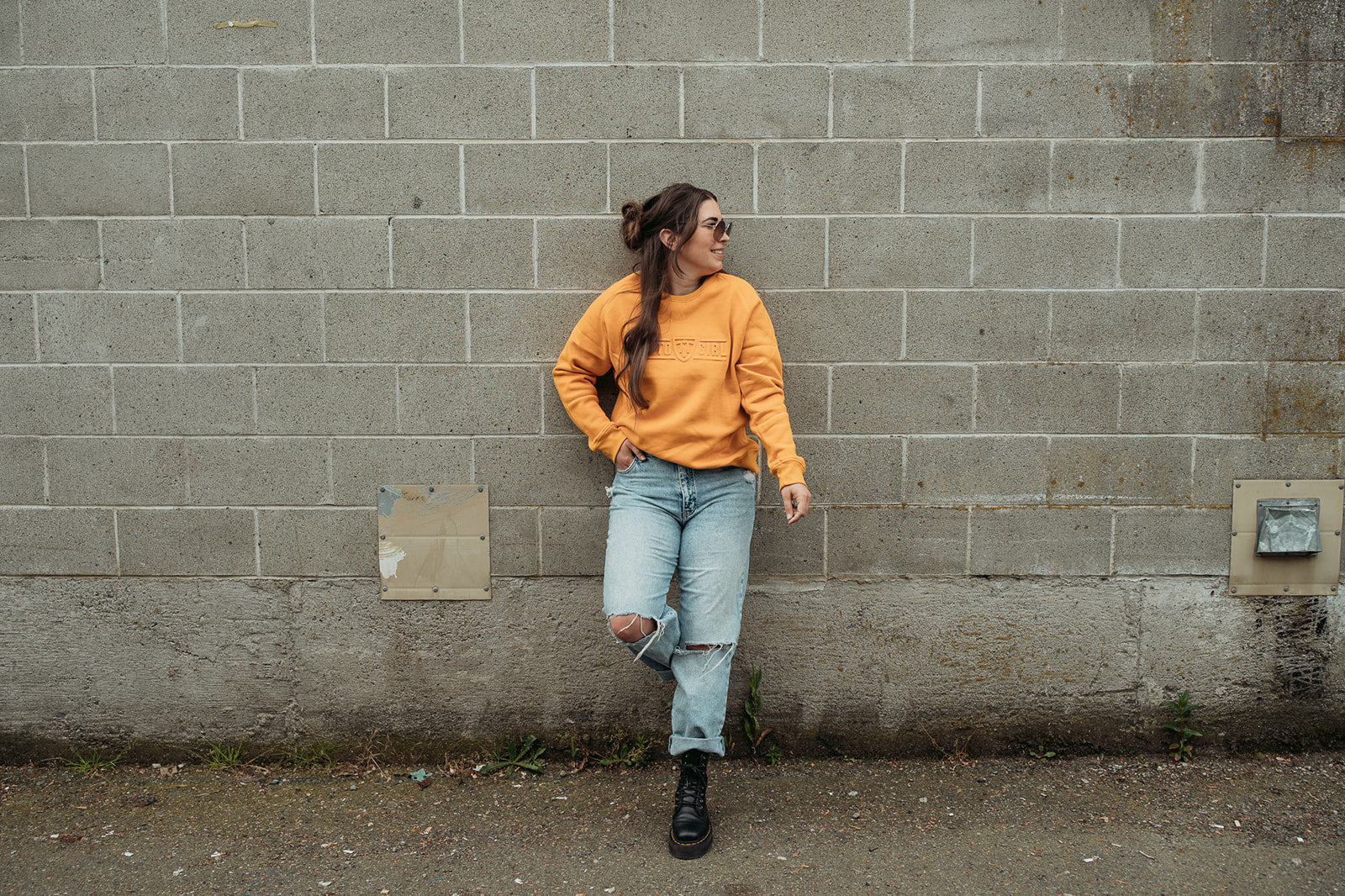 A young woman standing by a wall and wearing yellow colour lady sweatshirt with Moto Girl 3D logo