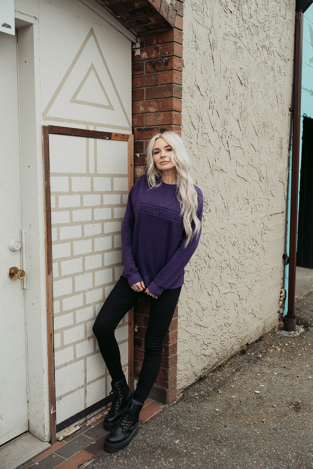 A young woman standing by a wall and wearing purple colour lady sweatshirt with Moto Girl 3D logo