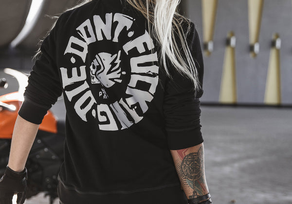A close up of the blond woman's back,  wearing Pando Moto black sweatshirt with while "Don't Fucking Die" motive 