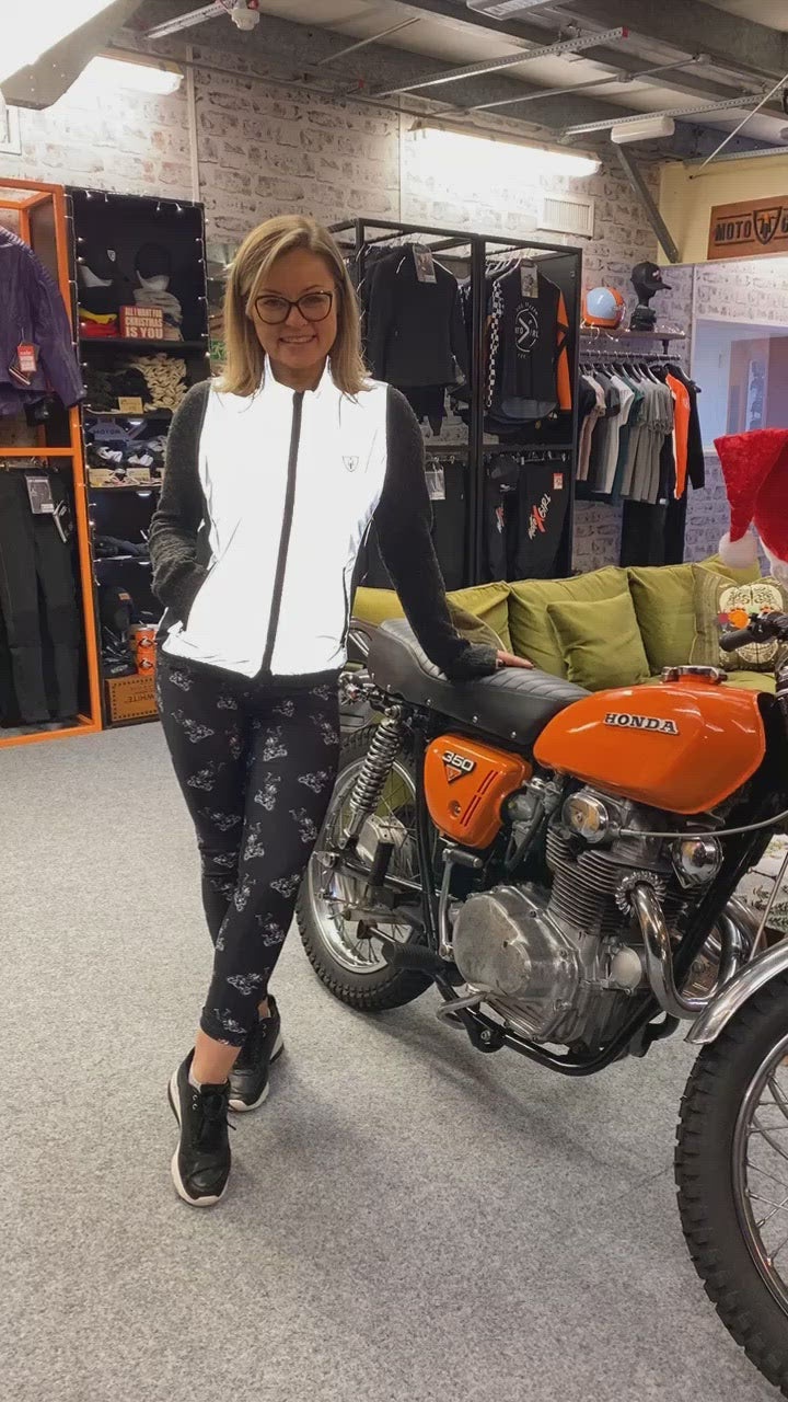 A blond smiling woman leaning on a honda motorcycle wearing reflective vest