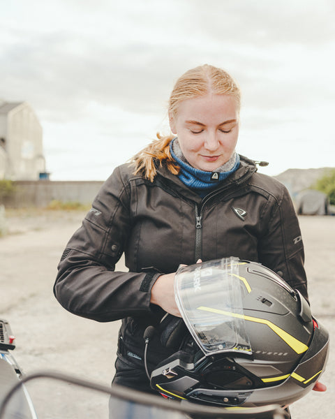 A young woman holding a helmet and wearing black motorcycle jacket 