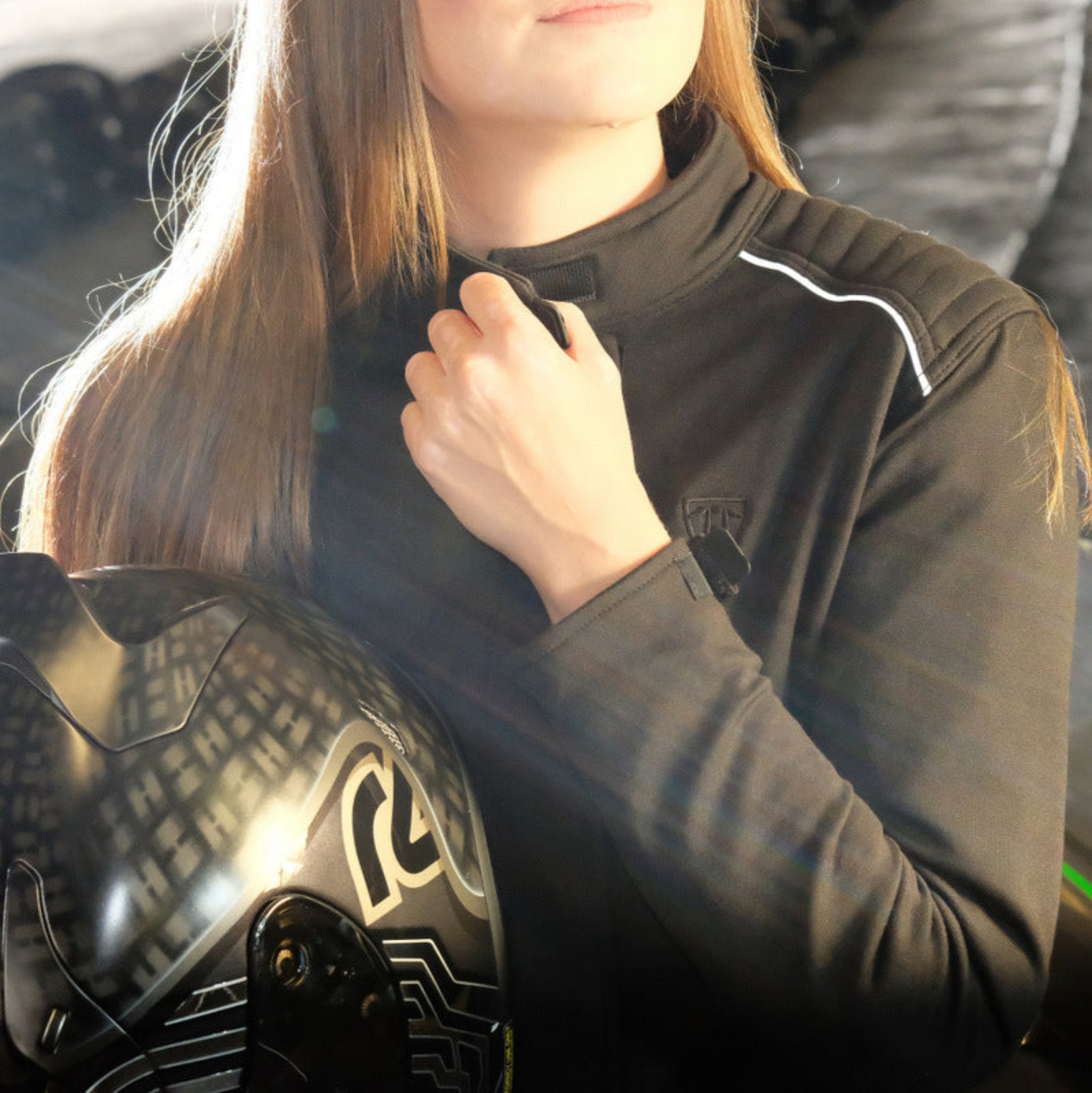 A woman closing her motorcycle jacket while holding a helmet