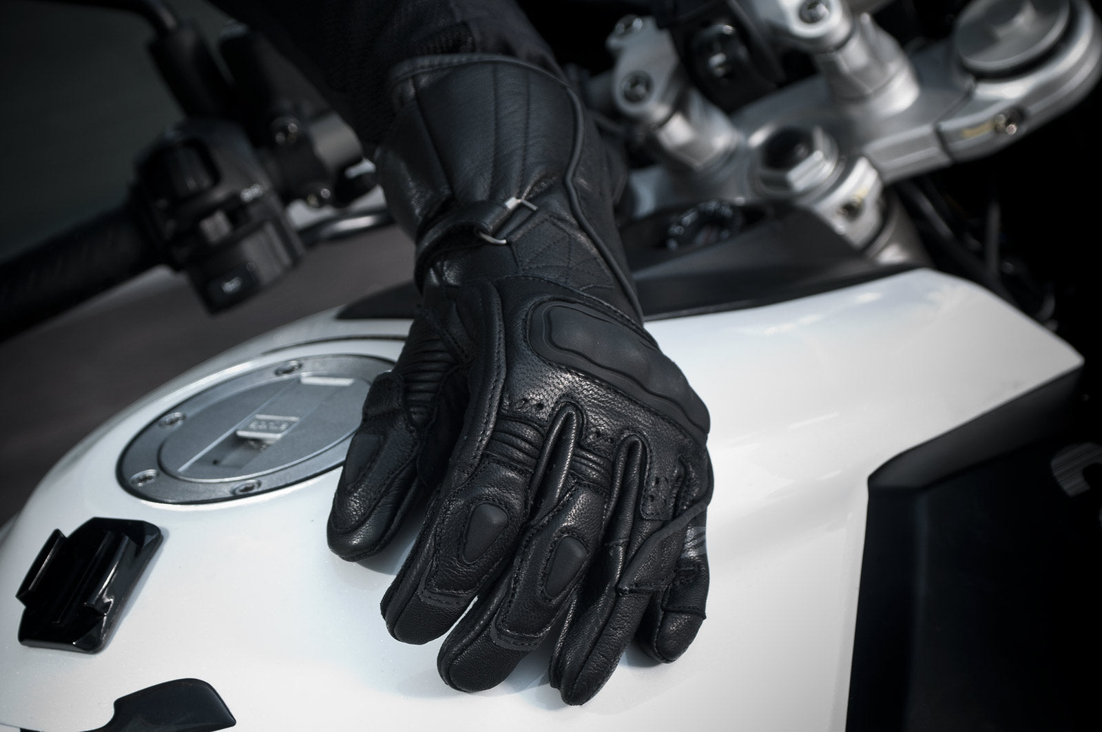 A  woman&#39;s hand with black waterproof motorcycle glove on a white motorcycle  tank 