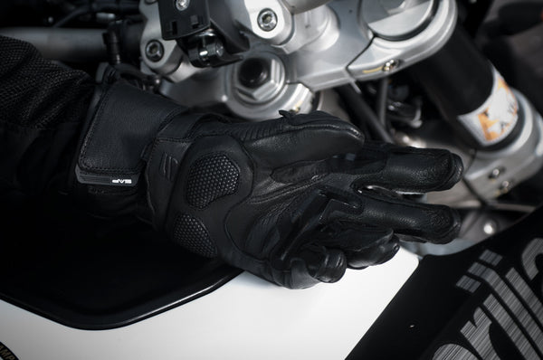 A  woman's hand with black waterproof motorcycle glove on a white motorcycle  tank 
