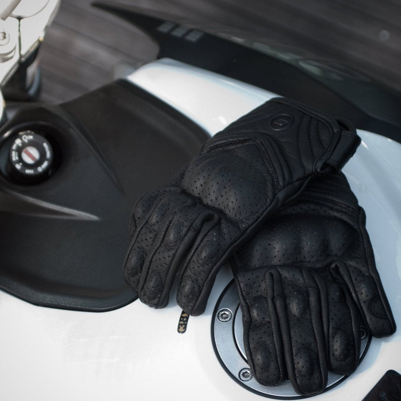 Black leather women's motorcycle gloves from Shima on a tank of a white motorcycle 