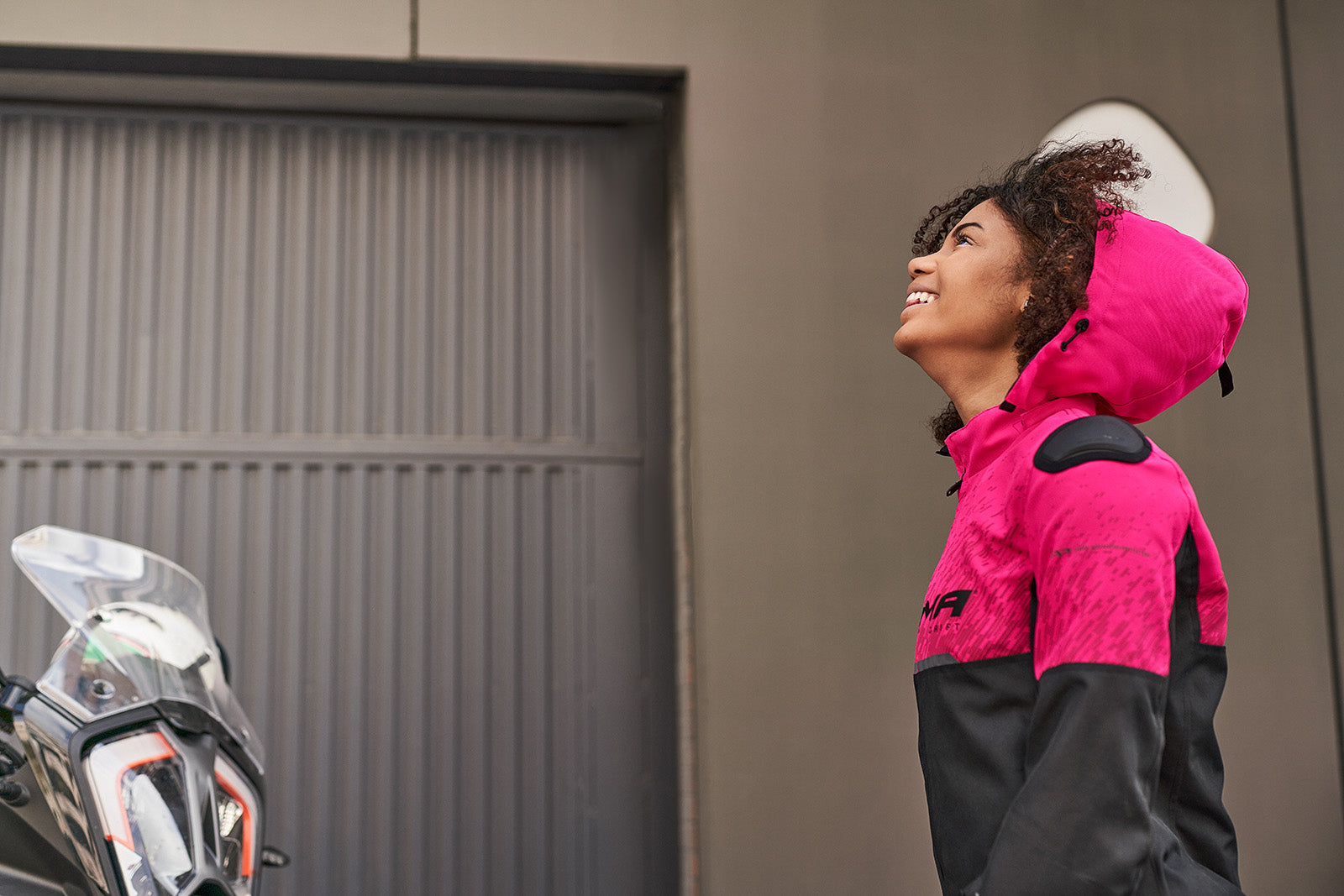 a smiling woman wearing pink DRIFT  motorcycle jacket from Shima with a hood