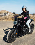 A young woman driving on a motorcycle wearing Classic retro black women's motorcycle jacket from Eudoxie