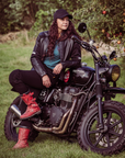 A woman leaning on her motorcycle wearing black leather motorcycle jacket and red boots 