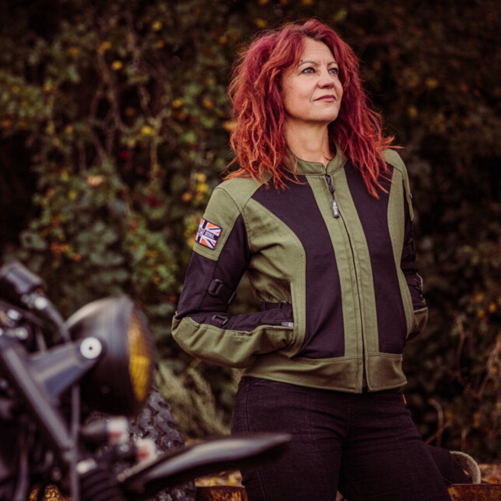 A women standing in front of a motorcycle wearing Women&#39;s motorcycle summer mesh jacket in black and green from Moto Girl