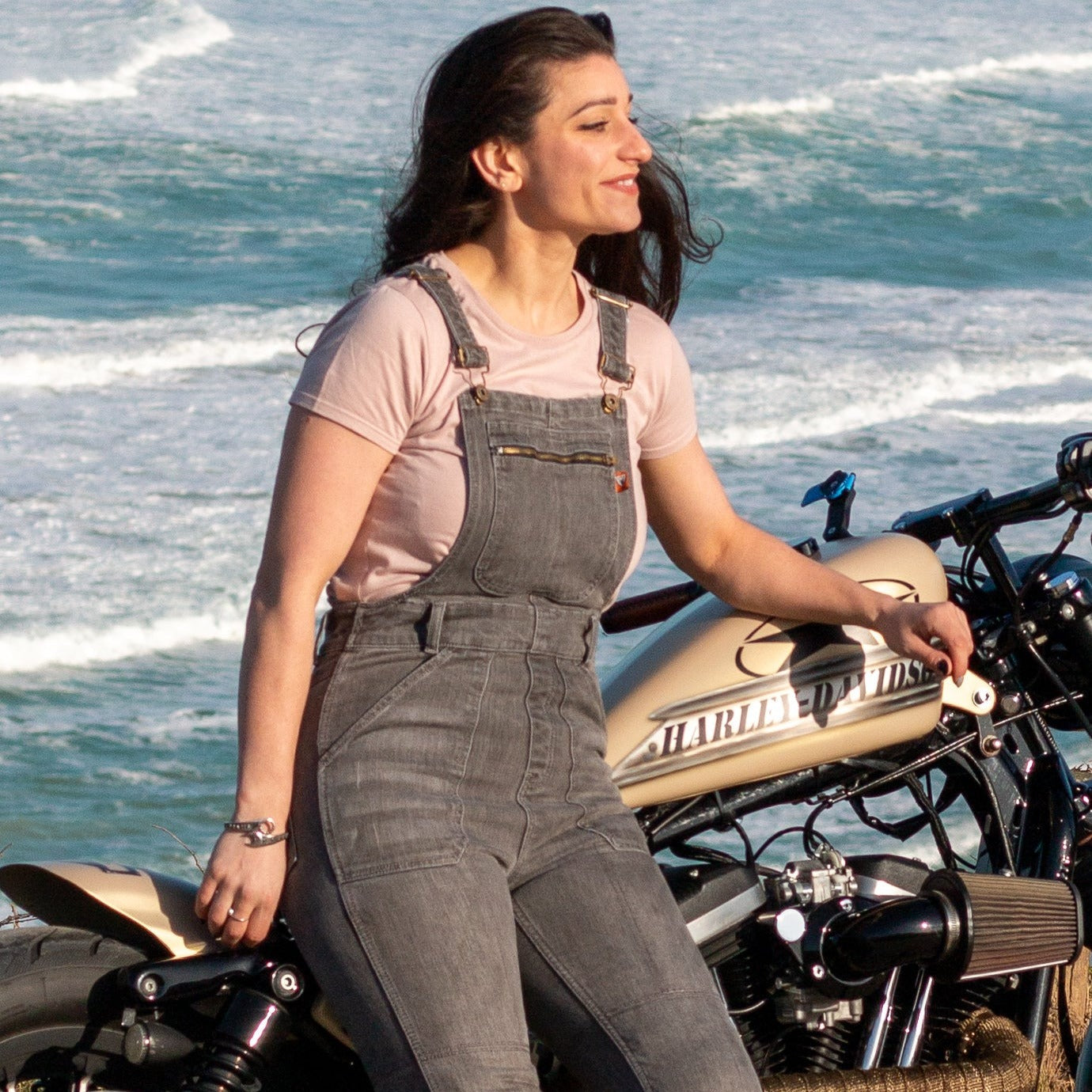 A woman by the beach with her motorcycle wearing grey women's motorcycle overall from Moto Girl