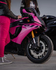 A woman wearing pink motorcycle trousers standing by a pink motorcycle