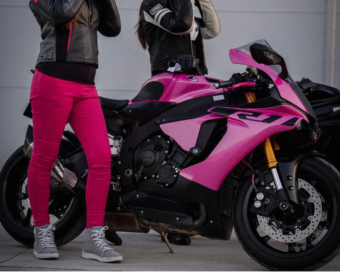 A woman wearing pink motorcycle trousers standing by a pink motorcycle