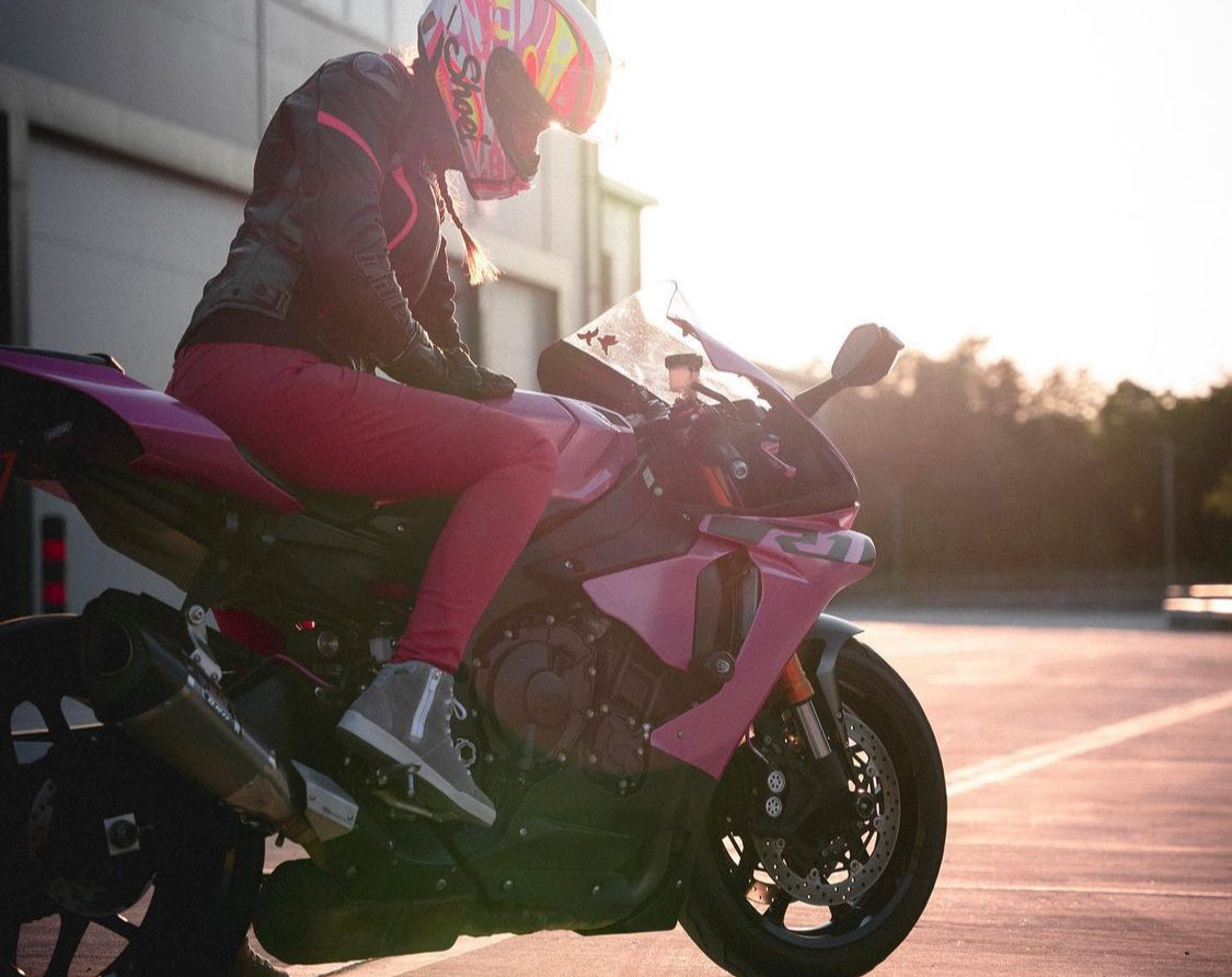 A woman wearing pink motorcycle trousers sitting on pink motorcycle