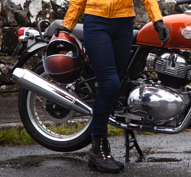 A woman wearing blue motorcycle jeans and carrying a helmet