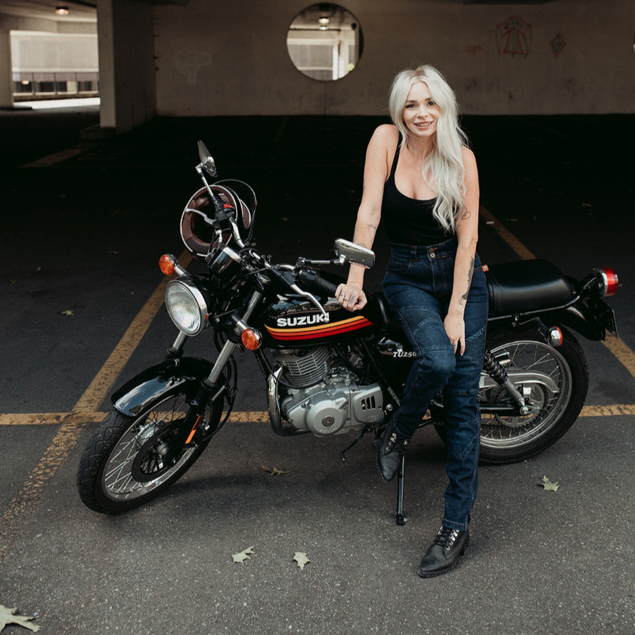 A tattooed woman on her Suzuki motorcycle wearing blue lady motorcycle jeans from Moto Girl.