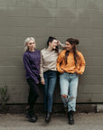 Three young women wearing colourful moto girl lady sweatshirts