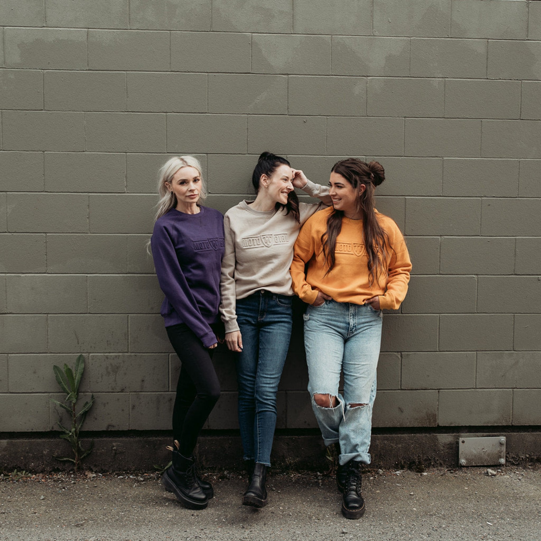 Three young women wearing colourful moto girl lady sweatshirts in the colors purple, sand and mustard yellow