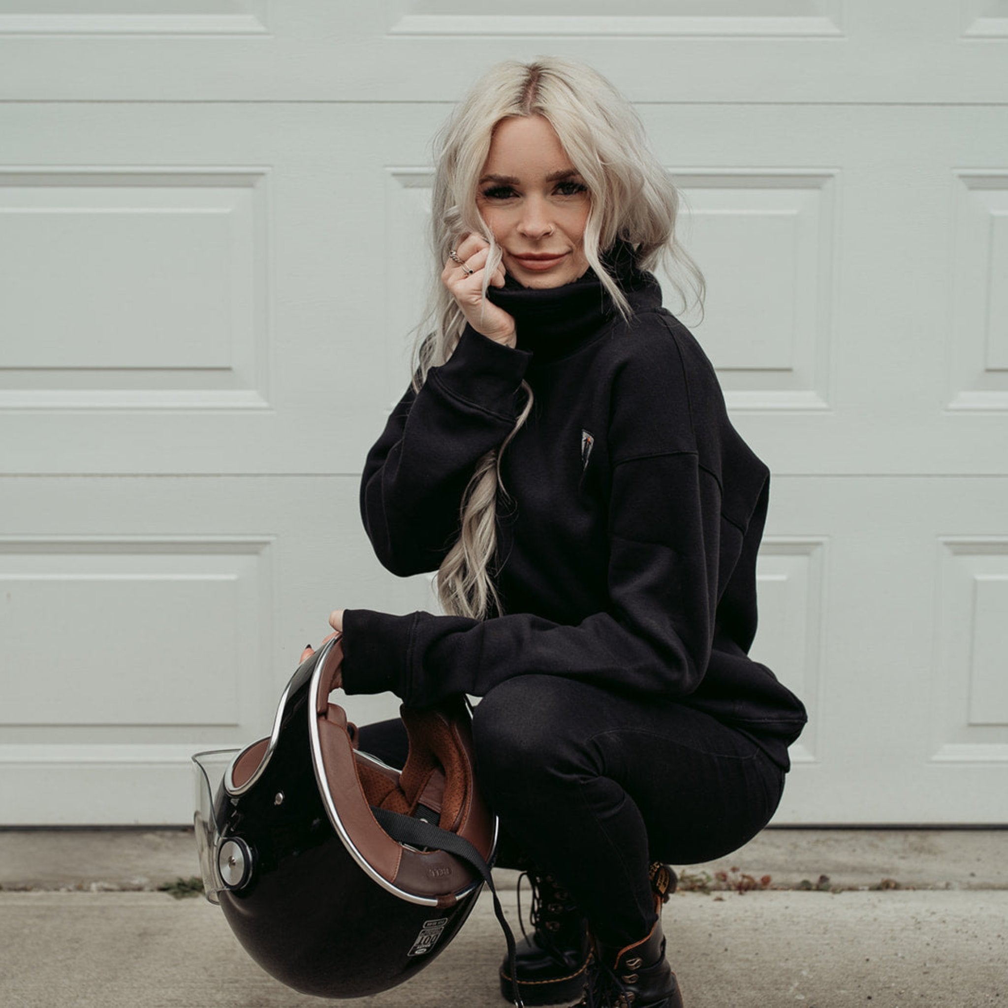 A young blond women wearing high neck black sweatshirt with motogirl logo in front