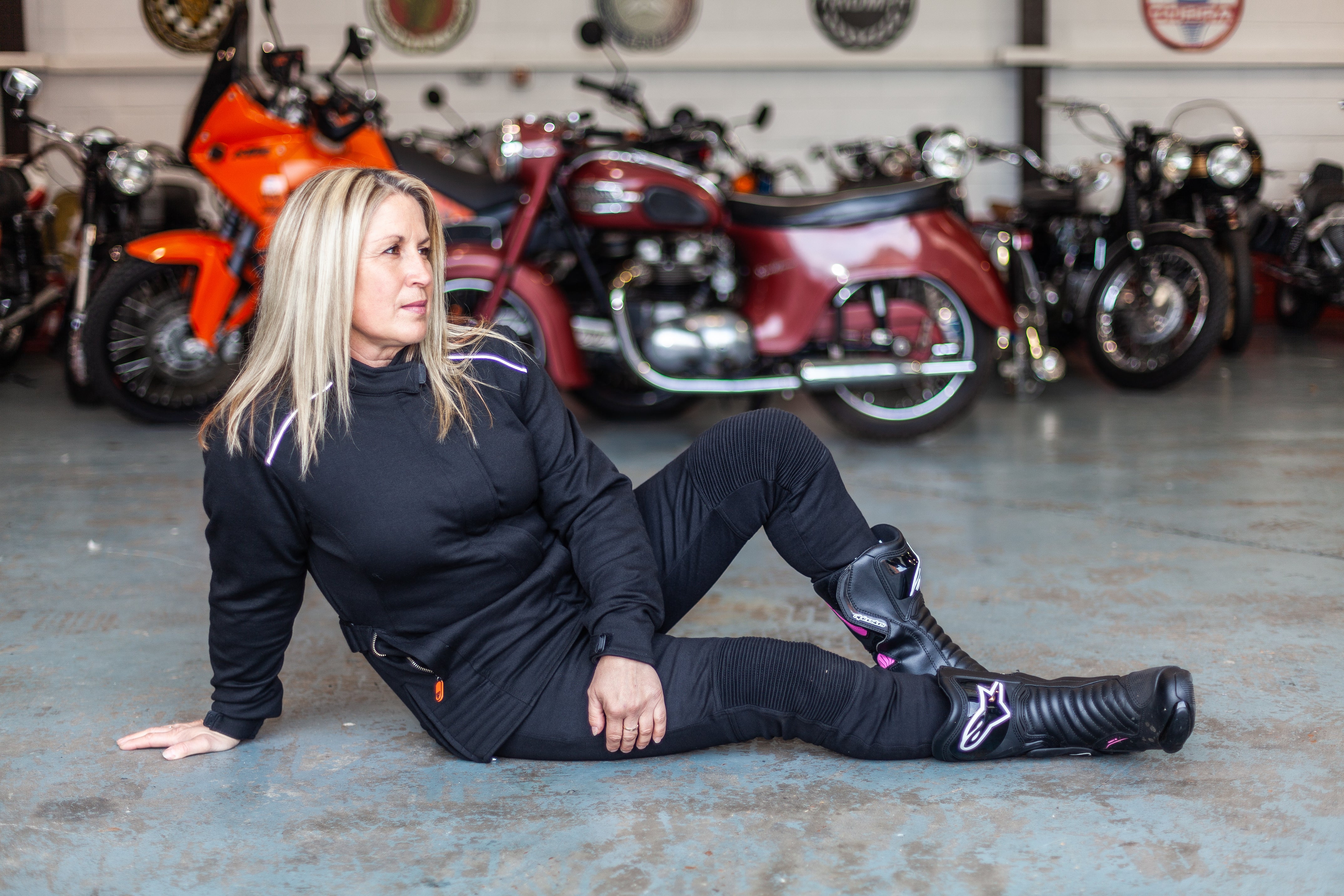 A blong woman sitting on the floor by motorcycles wearing women&#39;s motorcycle jacket from Moto Girl 