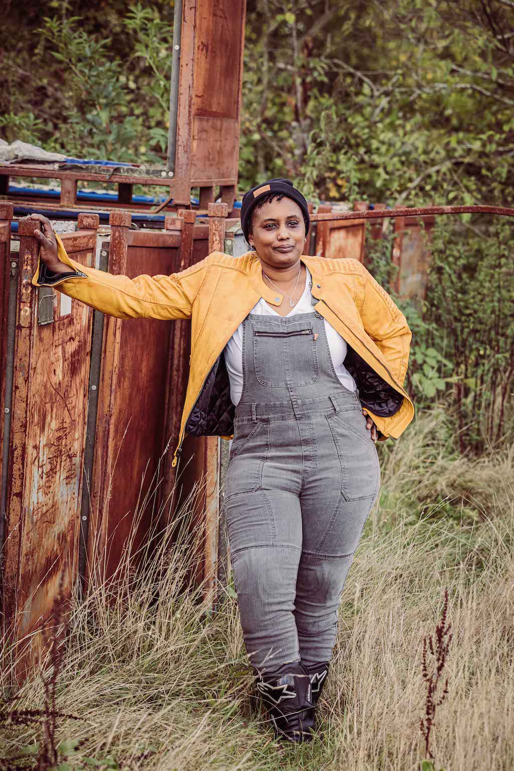A woman wearing grey motorcycle overall and yellow leather jacket standing by the metal container