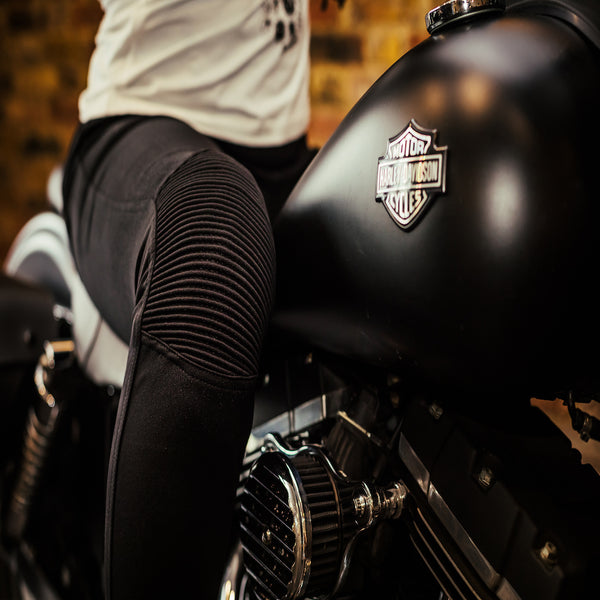 Close up of a woman's, sitting on the motorcycle and wearing black motorcycle leggings, knee