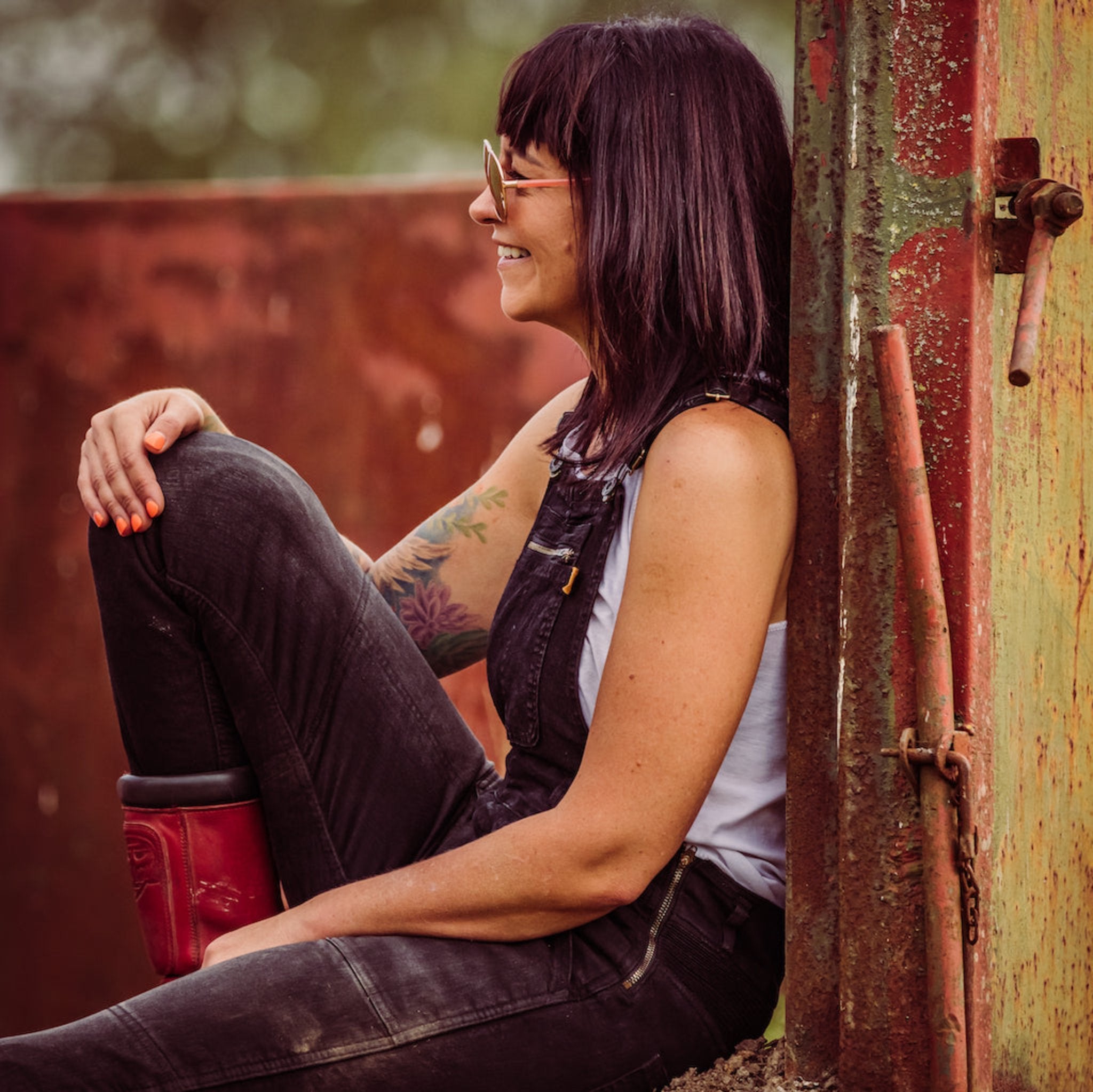 A siting and smiling dark haired woman wearing black motorcycle overall from MotoGirl