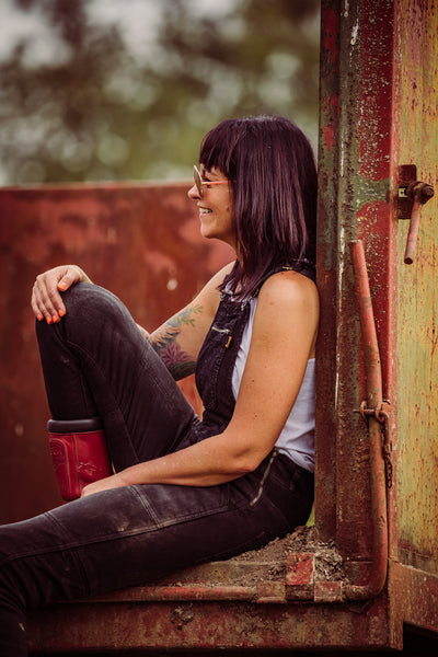 A siting and smiling dark haired woman wearing black motorcycle overall from MotoGirl