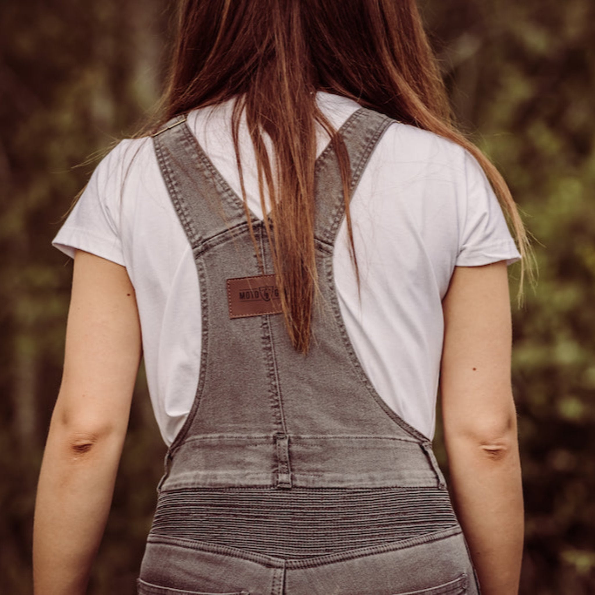 A back of a woman wearing white tshirt and grey motorcycle overall 