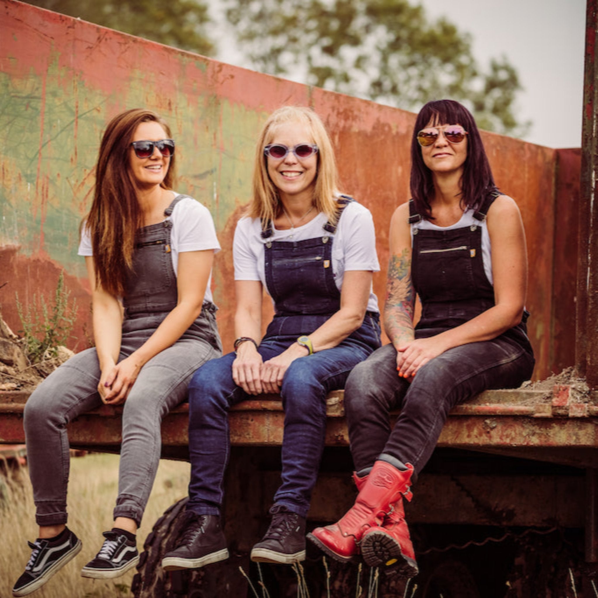 Three women wearing motorcycle overalls siting on the bed of a truck