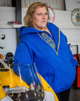A blond woman standing by a motorcycle wearing blue and yellow motorcycle hoodie from Moto Girl