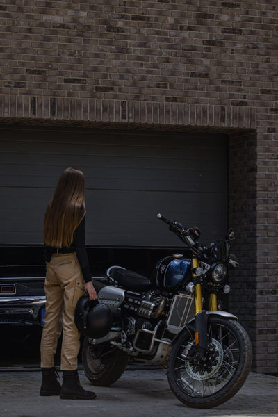 a woman standing by her motorcycle wearing beige mc pants
