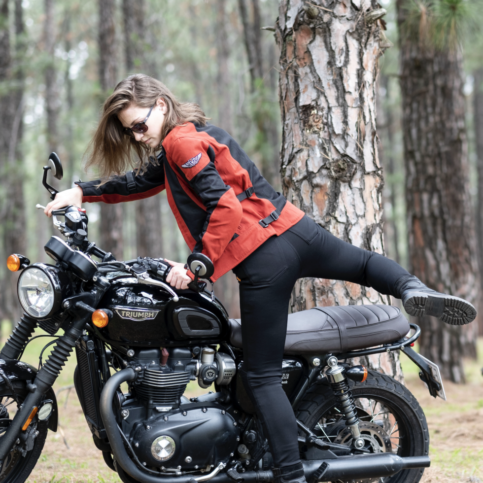 a young woman getting on a Triumph motorcycle wearing red and black women's motorcycle summer jacket from Moto Girl 