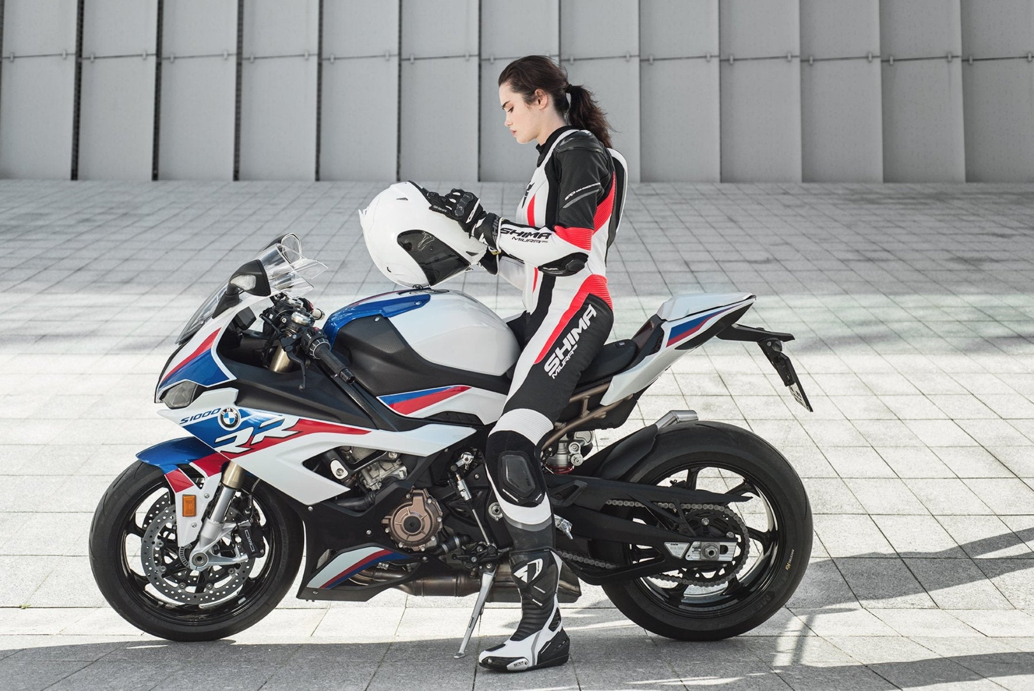 A young woman on a bmw racing motorcycle wearing Women&#39;s racing suit MIURA RS in black, white and fluo from Shima  