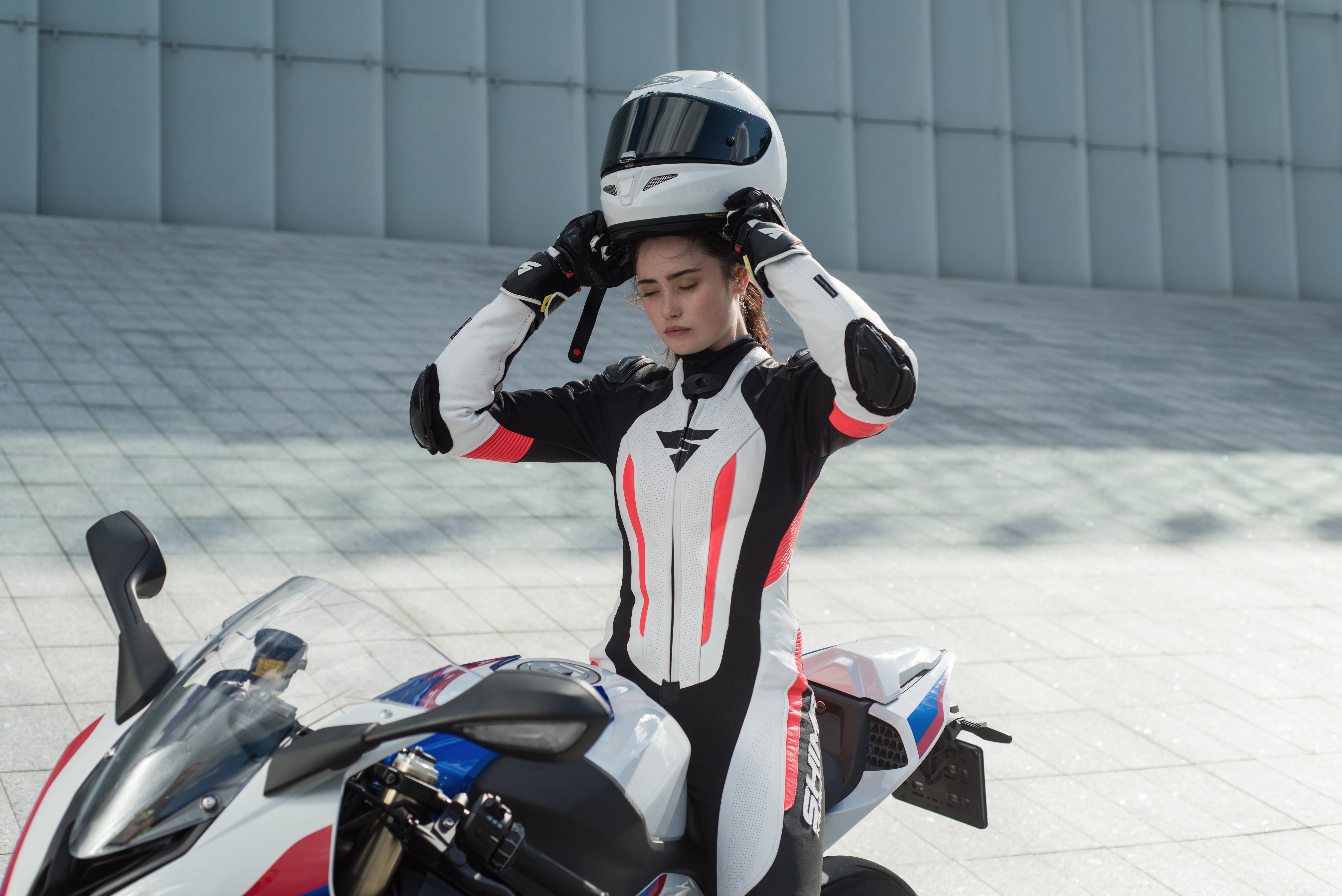 A woman putting her helmet on and wearing Women&#39;s racing suit MIURA RS in black, white and fluo from Shima 