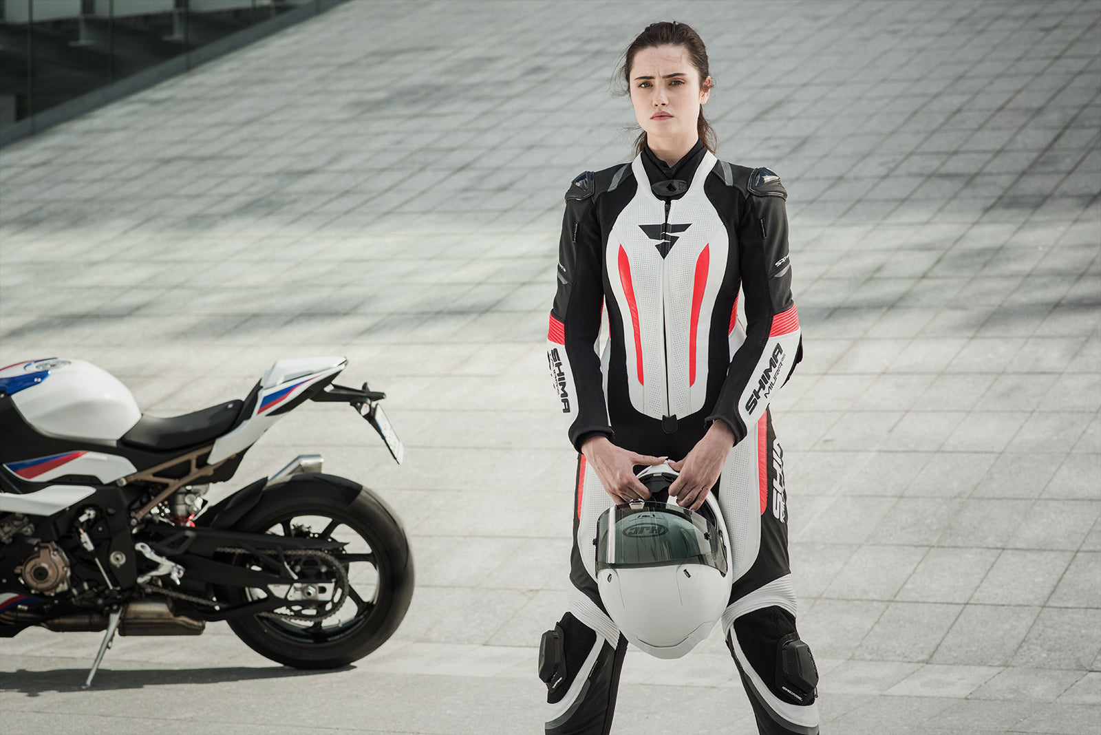 A young woman standing near a motorcycle wearing Women&#39;s racing suit MIURA RS in black, white and fluo from Shima 