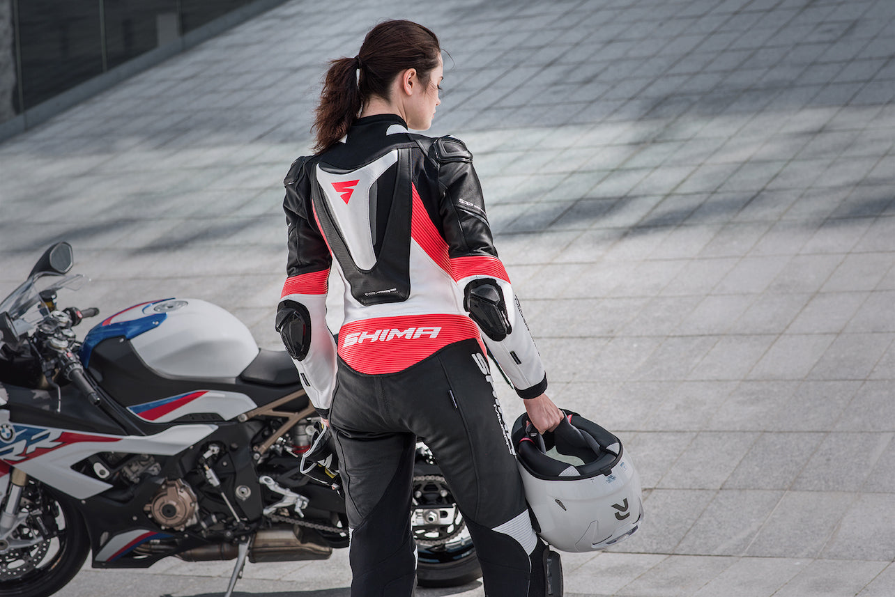 A woman standing near her motorcycle wearing Women&#39;s racing suit MIURA RS in black, white and fluo from Shima 
