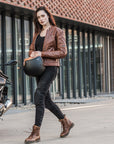 A young woman by a motorcycle wearing brown motorcycle leather jacket and brown women motorcycle boots from Shima