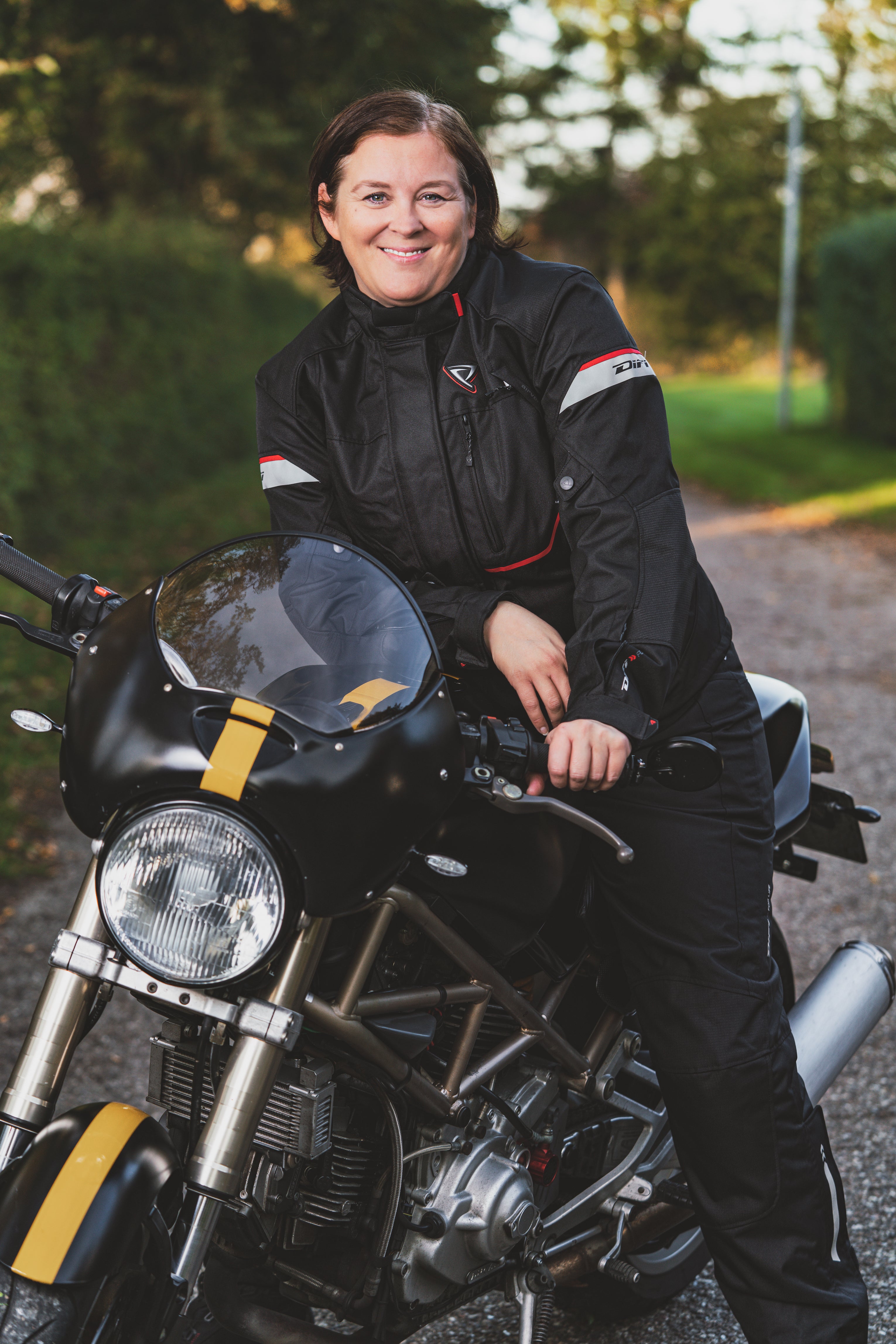 A smiling woman on a motorcycle wearing Difi textile women's motorcycle Nexia jacket and Cyclone pants