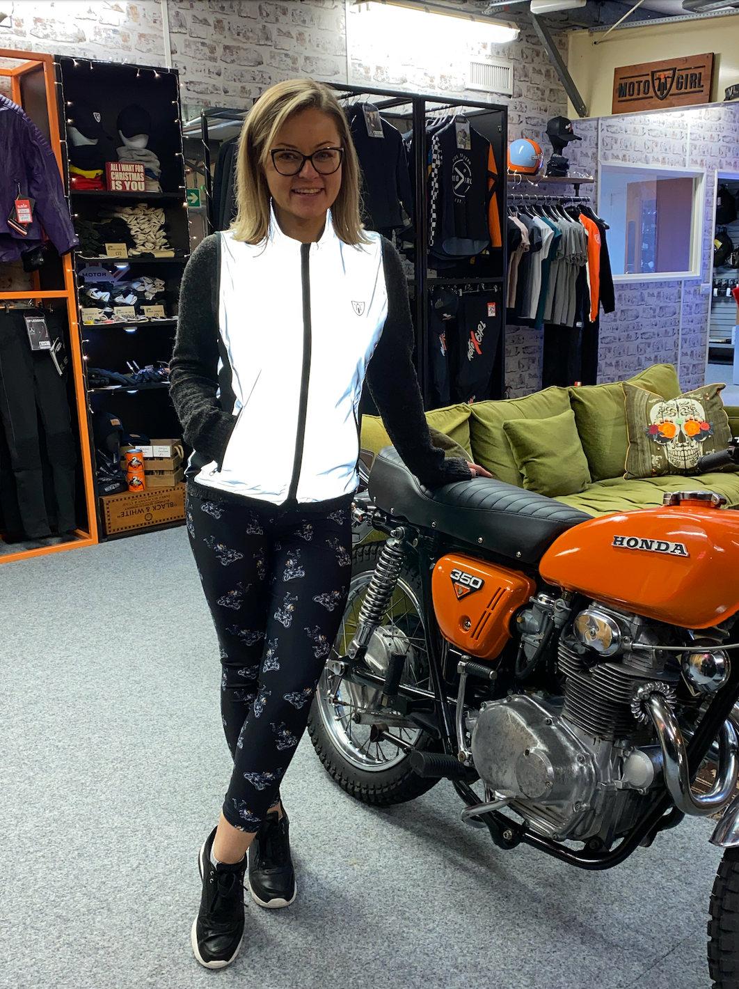 A blond smiling woman leaning on a motorcycle  wearing reflective vest