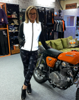 A blond smiling woman leaning on a motorcycle  wearing reflective vest