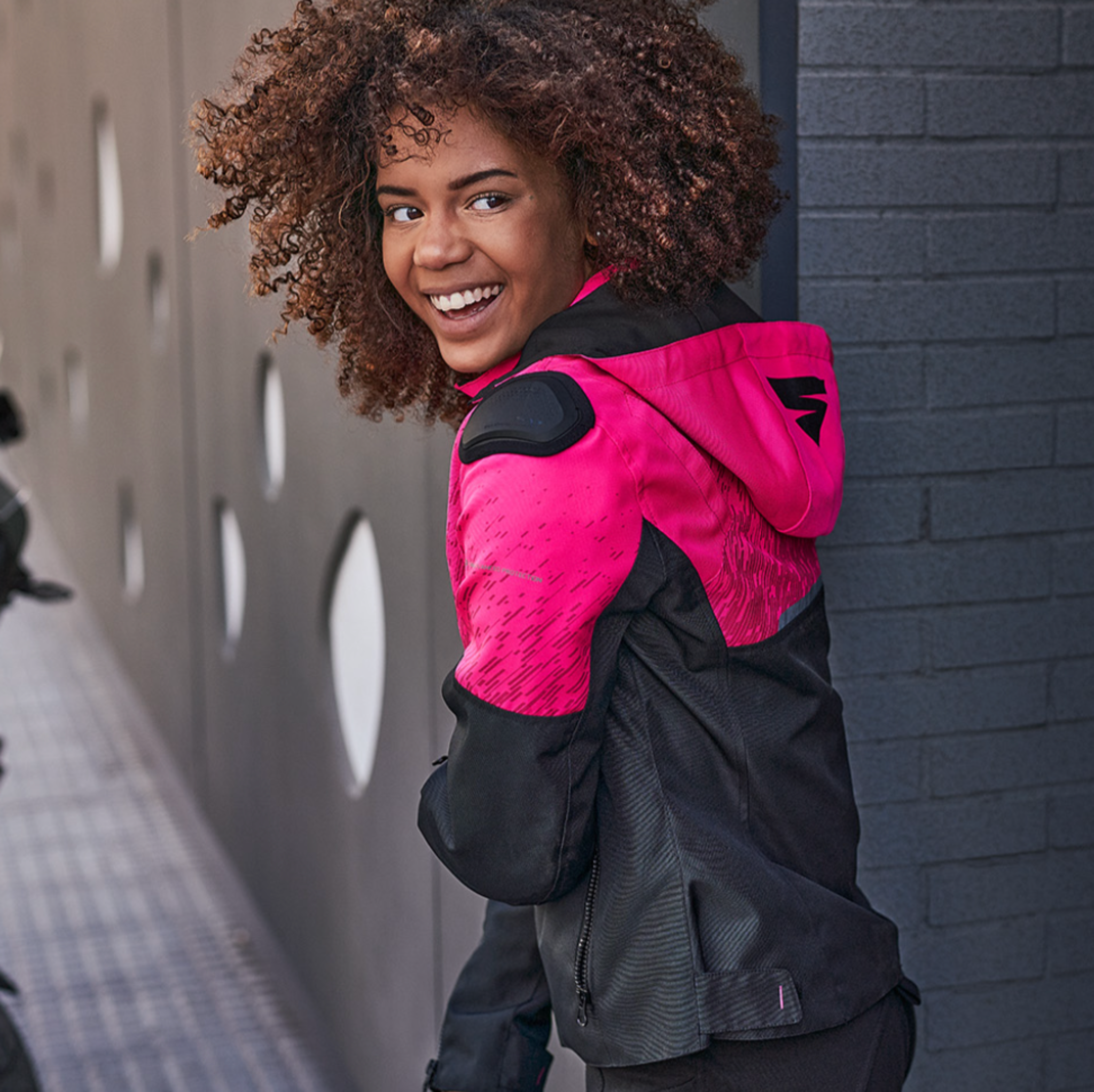 A young afroamerican woman wearing pink motorcycle jacket with the hood 