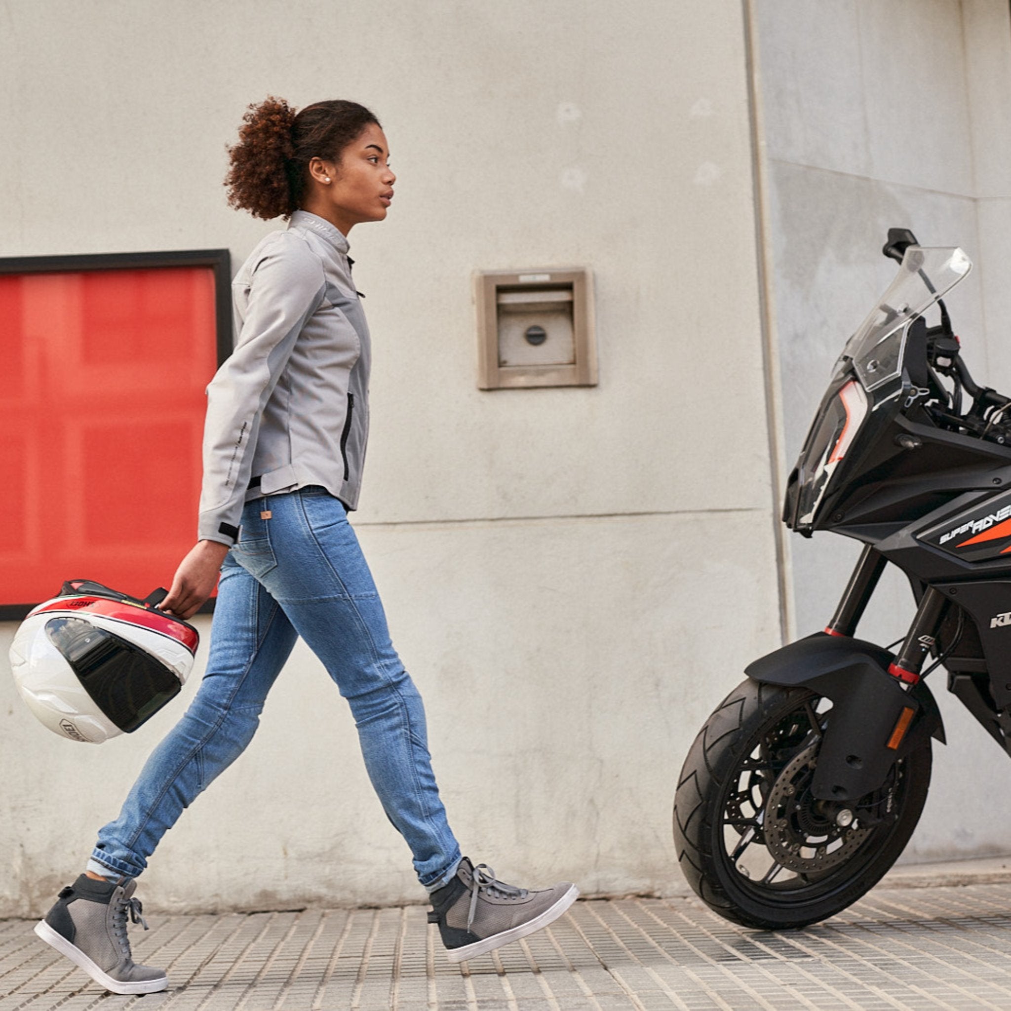 Young woman wearing Light blue motorcycle jeans for women walking towards her motorcycle